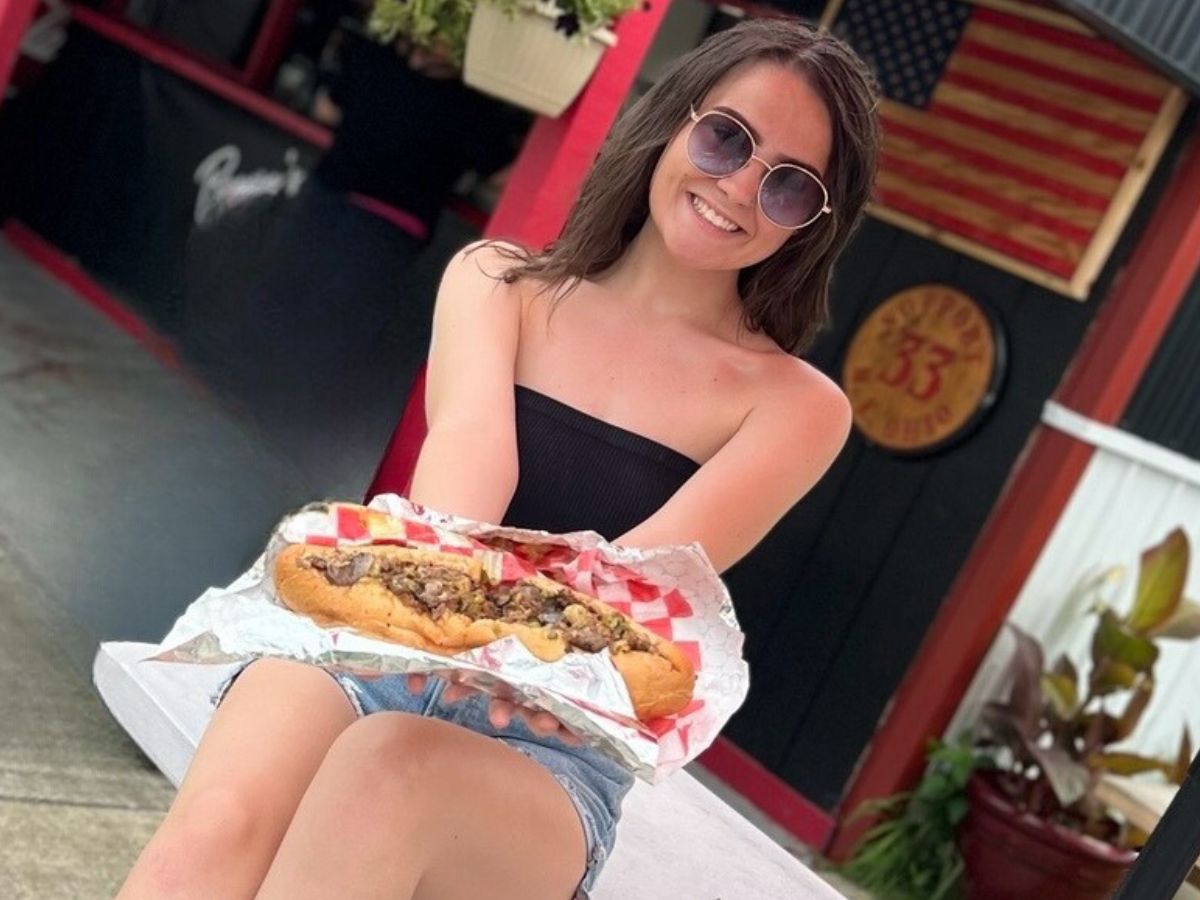 girl holding a cheesesteak on a patio