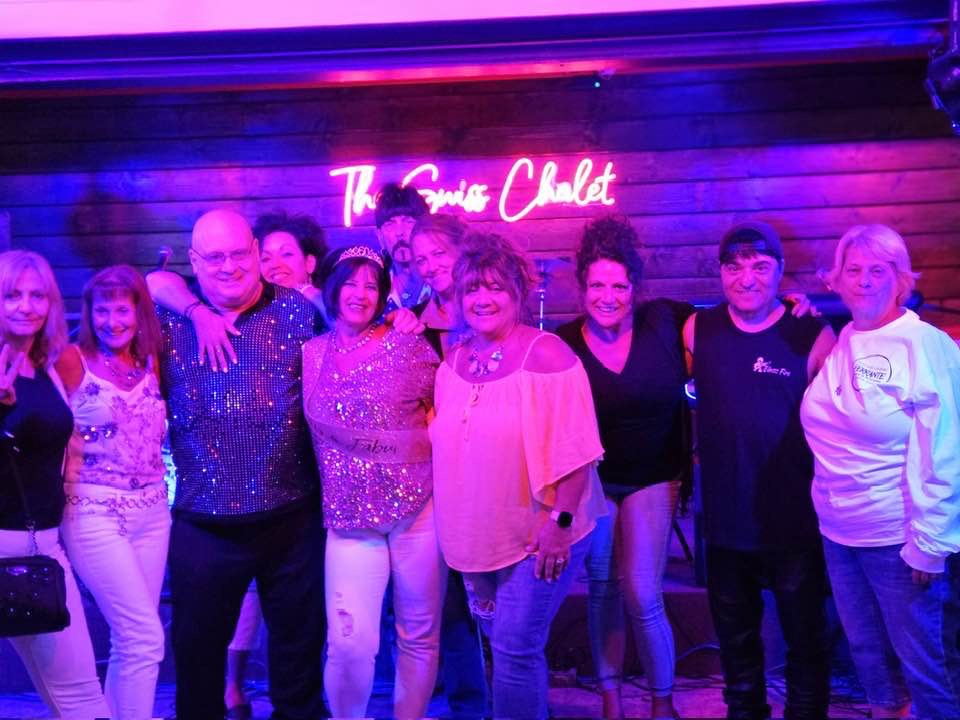 Band and friends in front of nightclub sign.